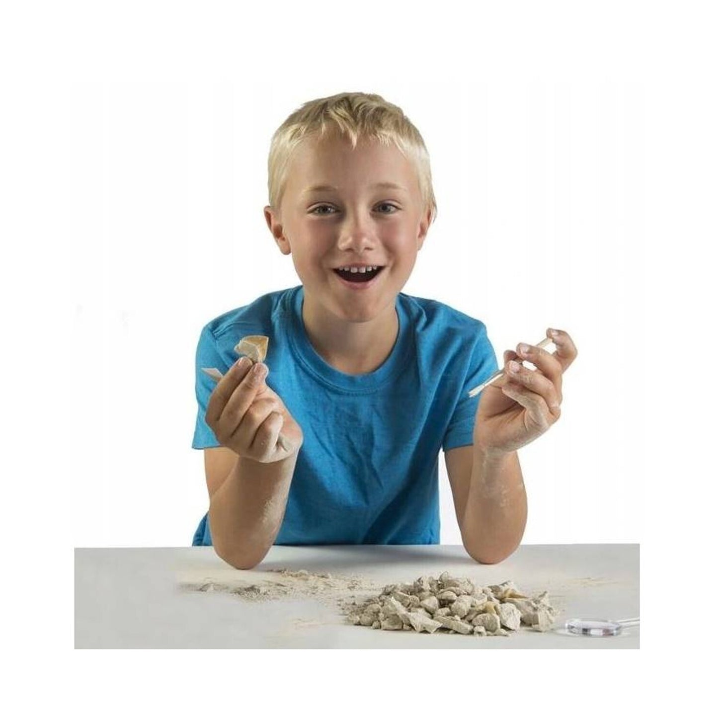 Smiling boy holds a piece of a fossil artifact and brush, using an archaeology excavation kit