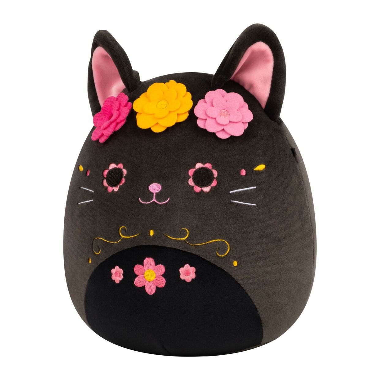A dark plush cat Squishmallow featuring pink inner ears, a crown of bright felt flowers, and embroidered Day of the Dead sugar skull details