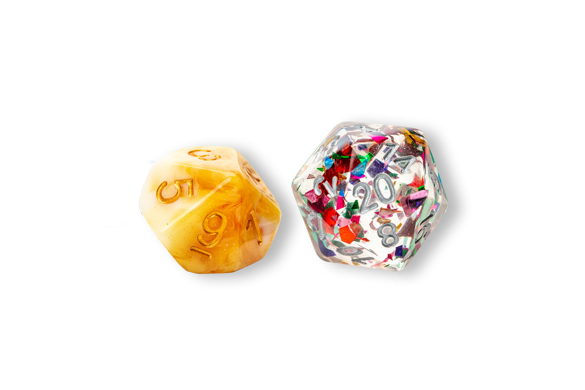 Two d20 dice, one translucent yellow with gold numbers and glitter, the other clear with confetti and silver numbers