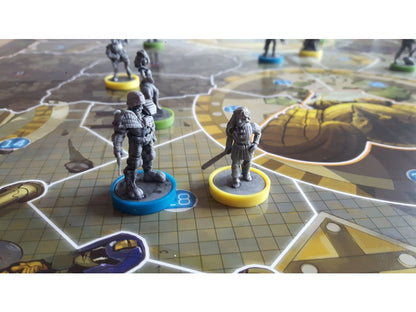 Two grey fantasy miniatures, an armored male and a female with a sword, on colored bases on a game board