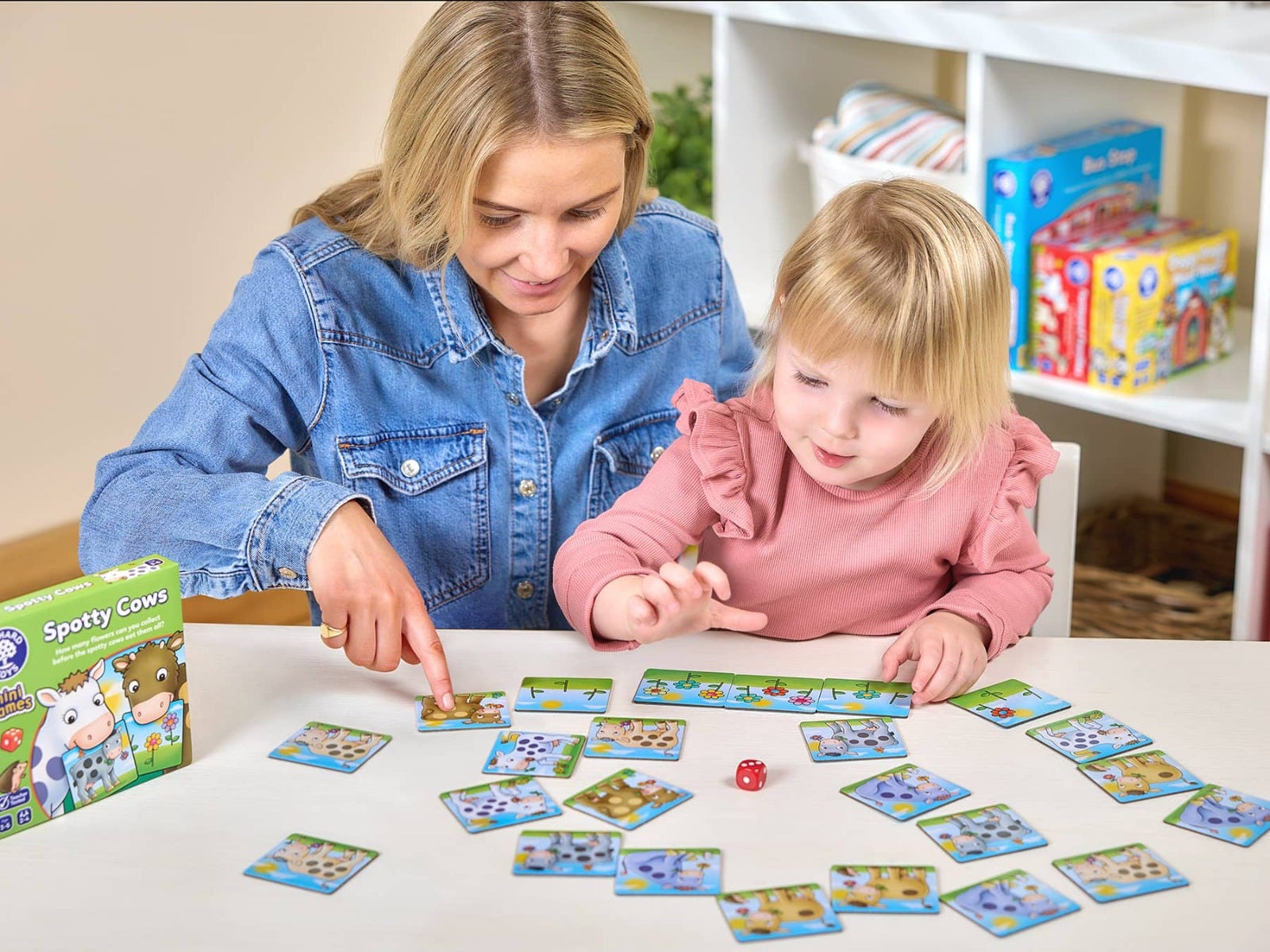 Mother and toddler playing the Spotty Cows mini game, pointing at cow tiles and a flower track on a white table