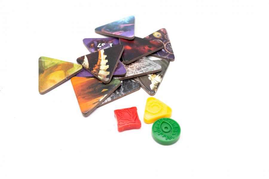 Etherfields 5th Player Expansion game components featuring multiple triangular-shaped cardboard tokens with various colorful artwork alongside one red square and two yellow and green plastic tokens