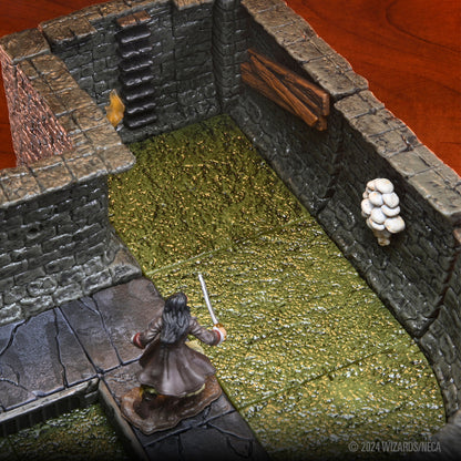 A miniature woman with long hair and a sword stands on a stone path looking into a dungeon room with a textured green floor and stone walls