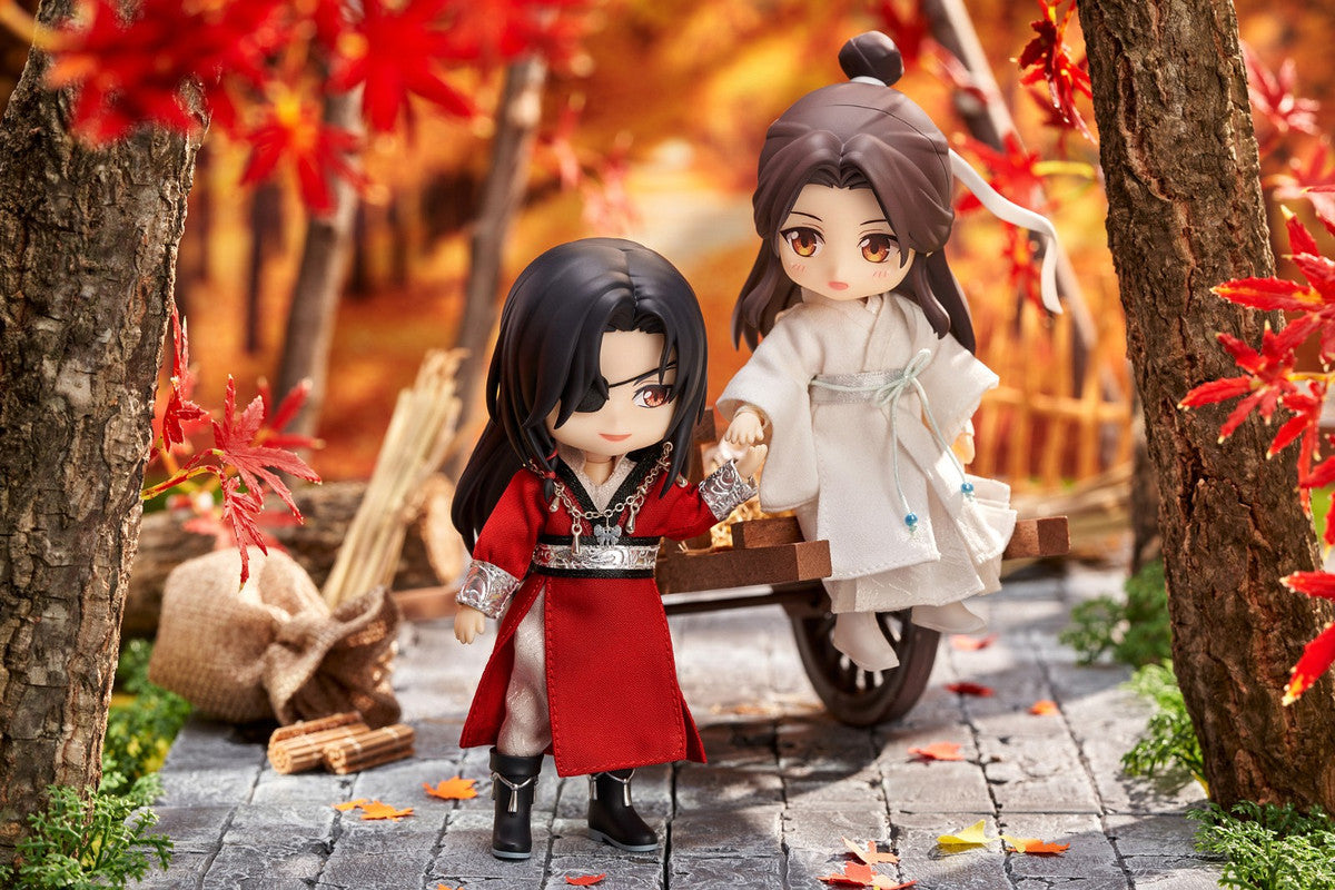Nendoroid figures of Hua Cheng in red and Xie Lian in white standing by a cart in an autumn forest scene with red maple leaves