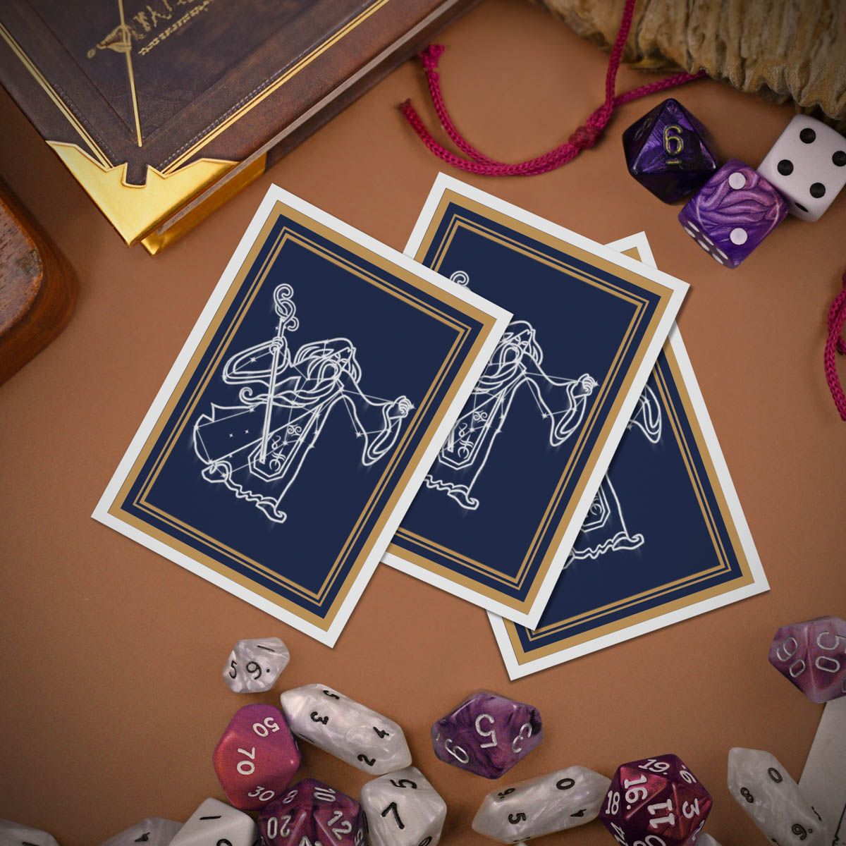 Blue fantasy game cards featuring a white line art mage, surrounded by scattered RPG dice and a gold-edged rulebook