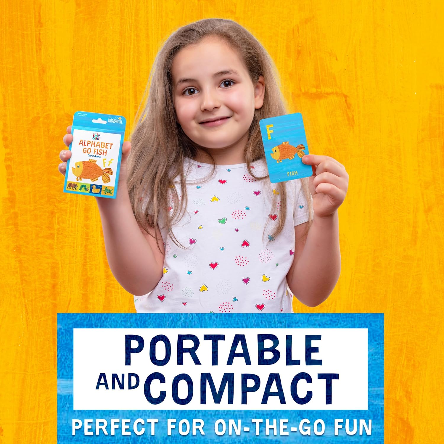 Smiling girl holding the Eric Carle Alphabet Go Fish card game box and a learning card showing the letter F for Fish