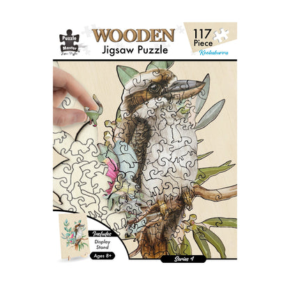 117-piece wooden jigsaw puzzle featuring a Kookaburra bird design, partially assembled, with a hand placing a dinosaur-shaped piece