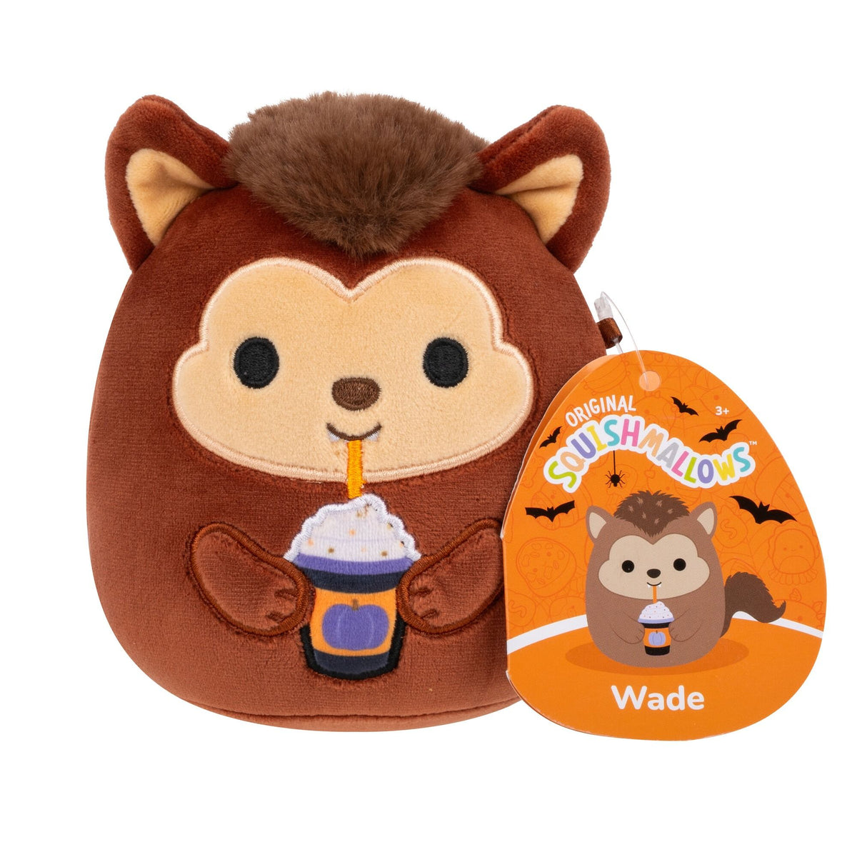 A brown Squishmallow plush toy resembling a fuzzy werewolf holds a purple Halloween drink with whipped cream and an orange straw, with a festive tag attached