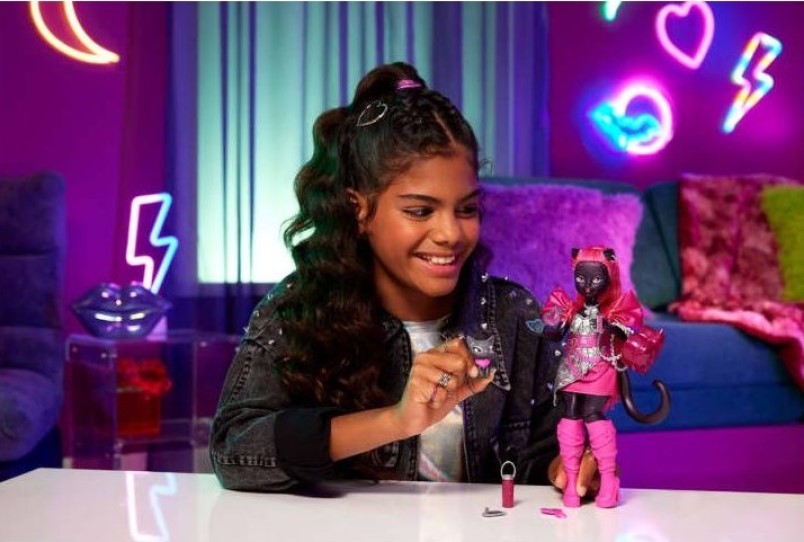 Smiling girl plays with a black cat doll in a pink outfit, holding a cat charm. Vibrant purple room with neon lights and decorative shapes