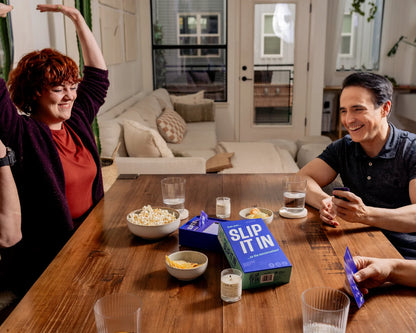 A group of friends playing the "Slip It In" card game; a woman cheers with her arms raised