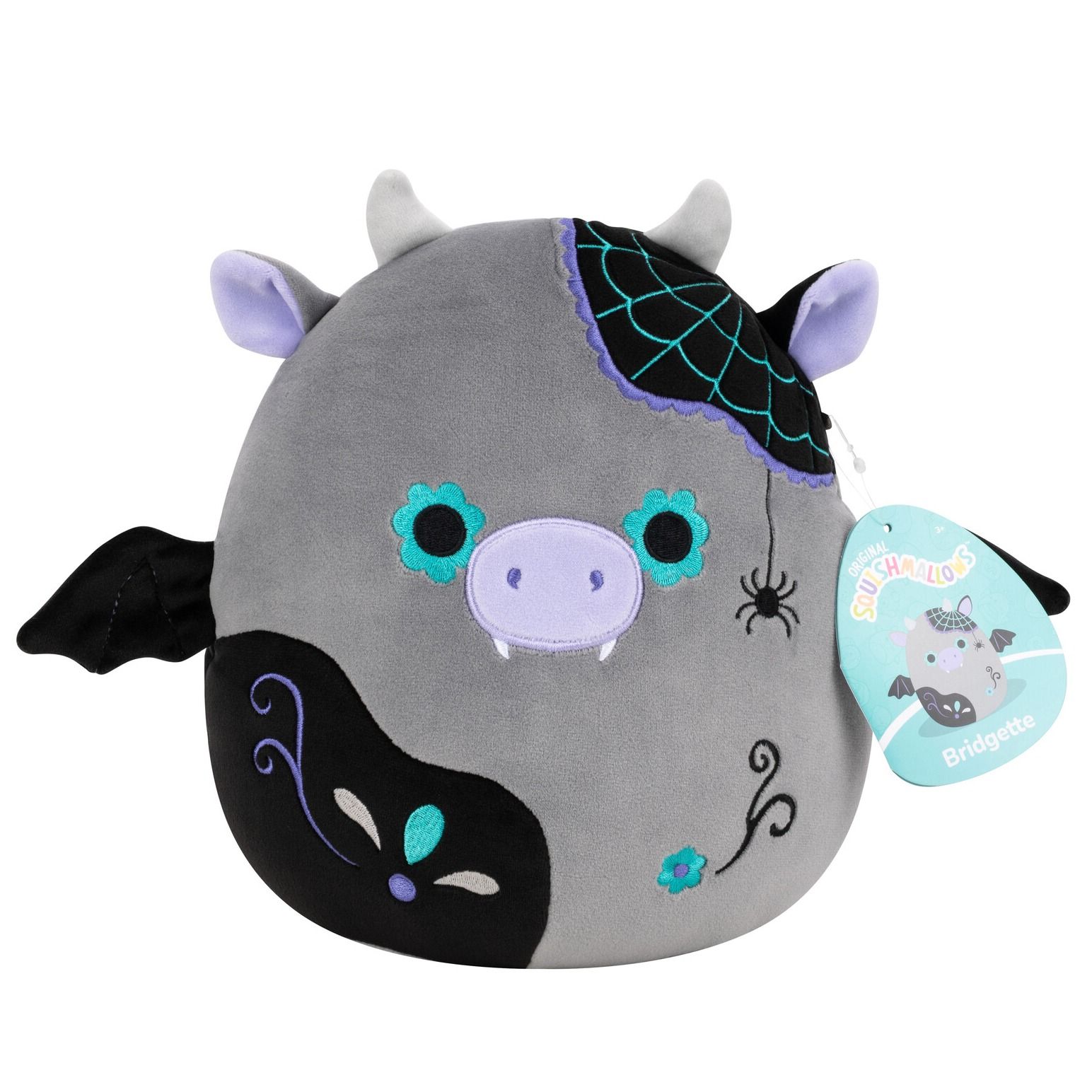 Bridgette the Squishmallow is a gray cow plush with bat wings, fangs, a purple and black spiderweb patch, and a dangling spider on its body