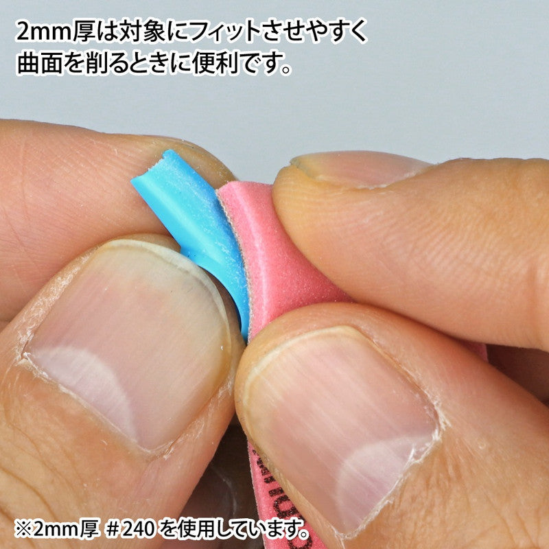 Close-up of hands using a pink sanding sponge to sand a flexible blue strip, bending to a curve