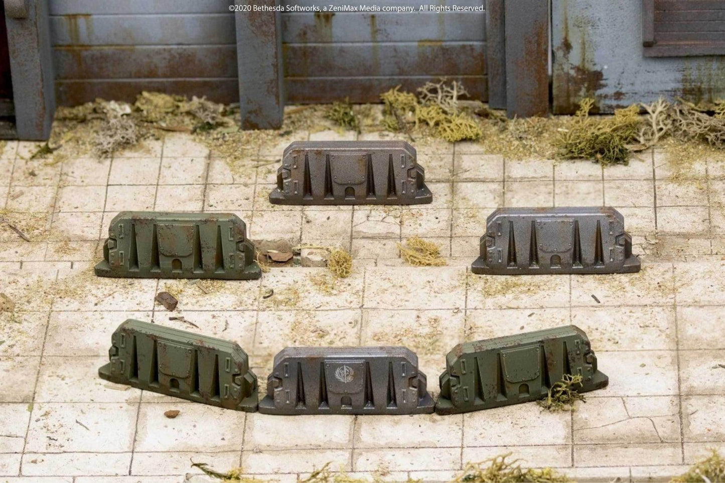 Six weathered green and grey miniature wargaming barriers arranged in a circle on a dirty tiled ground