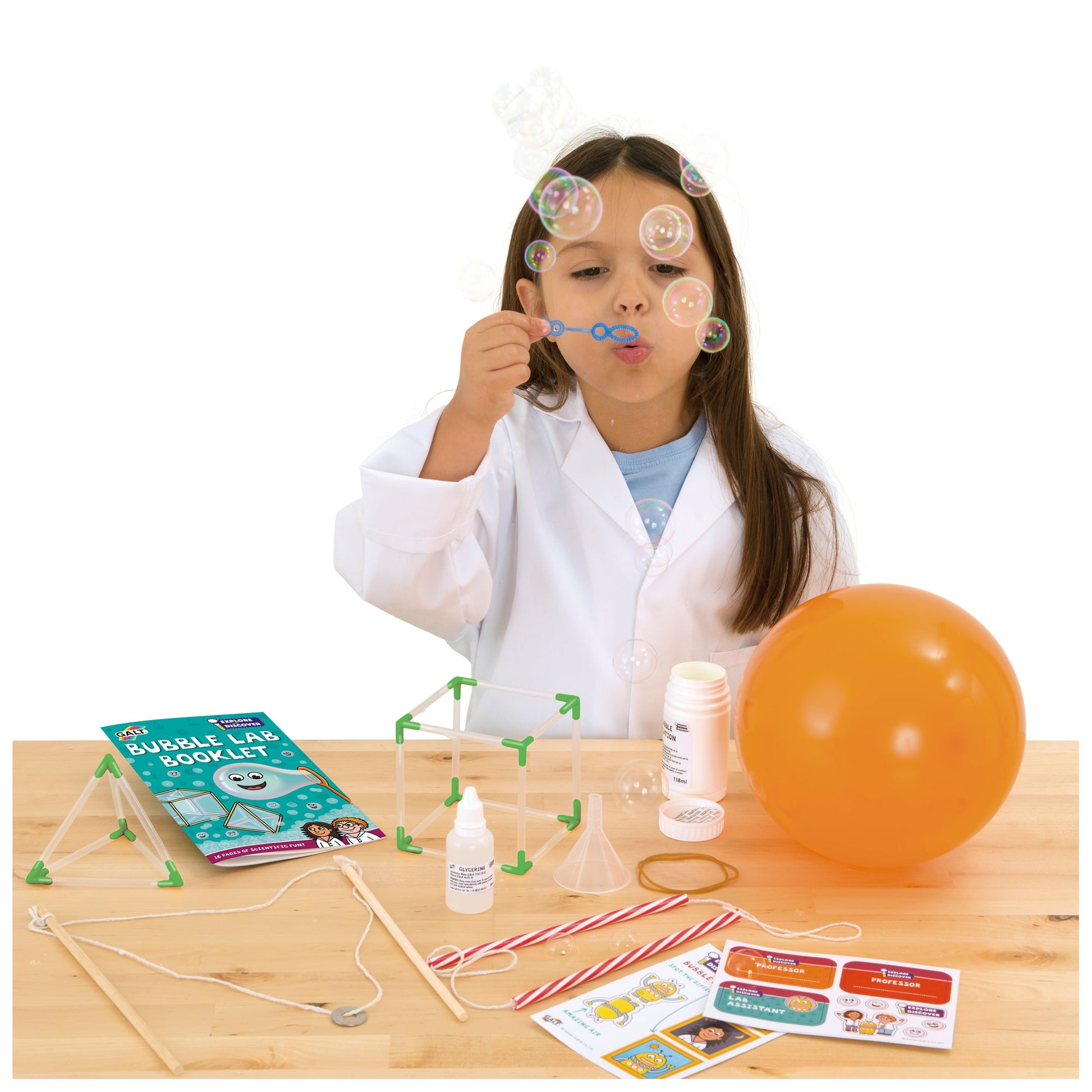 Child in a lab coat blowing bubbles from a bubble science kit laid out on a table