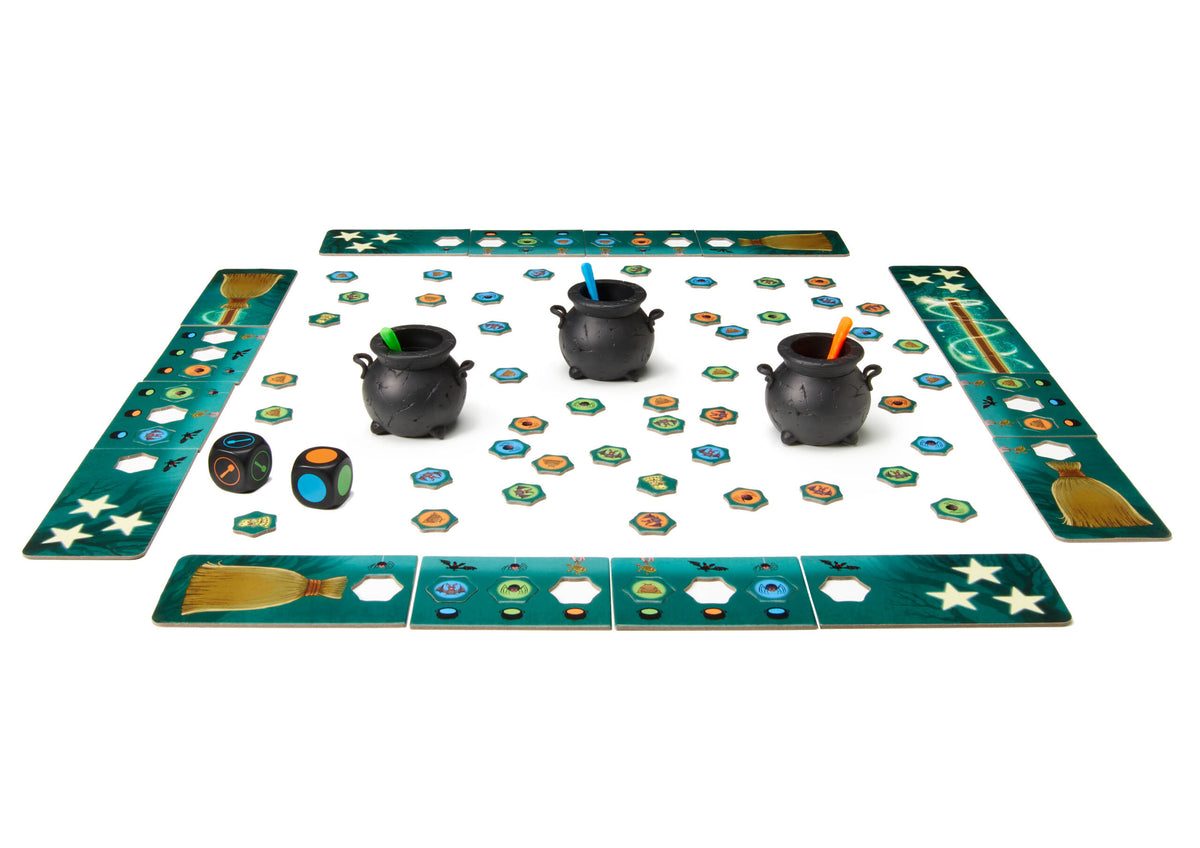 Witch-themed board game setup: four green paths, three black cauldrons with colorful stirrers, hexagonal ingredient tokens, and two dice on white