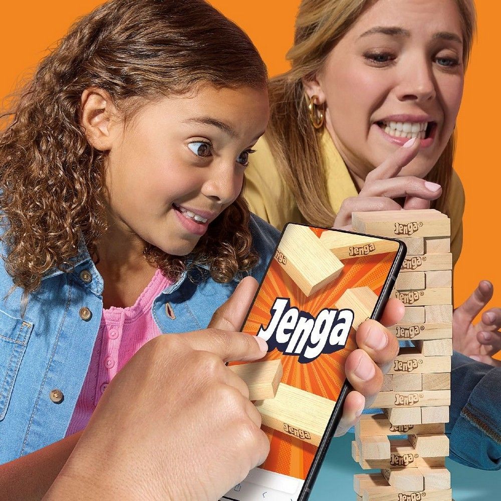 Young girl plays Jenga on a smartphone; adult woman anxiously watches a nearby Jenga tower