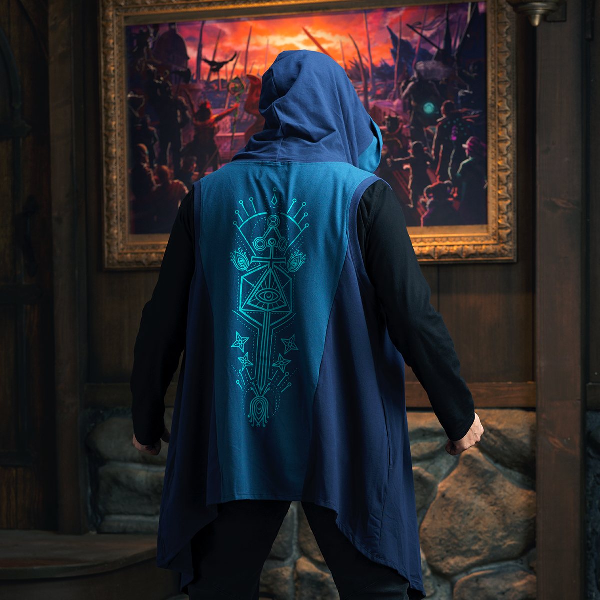 Person from behind in a hooded blue vest with a geometric eye design, looking at a large painting of an orange-skied battle