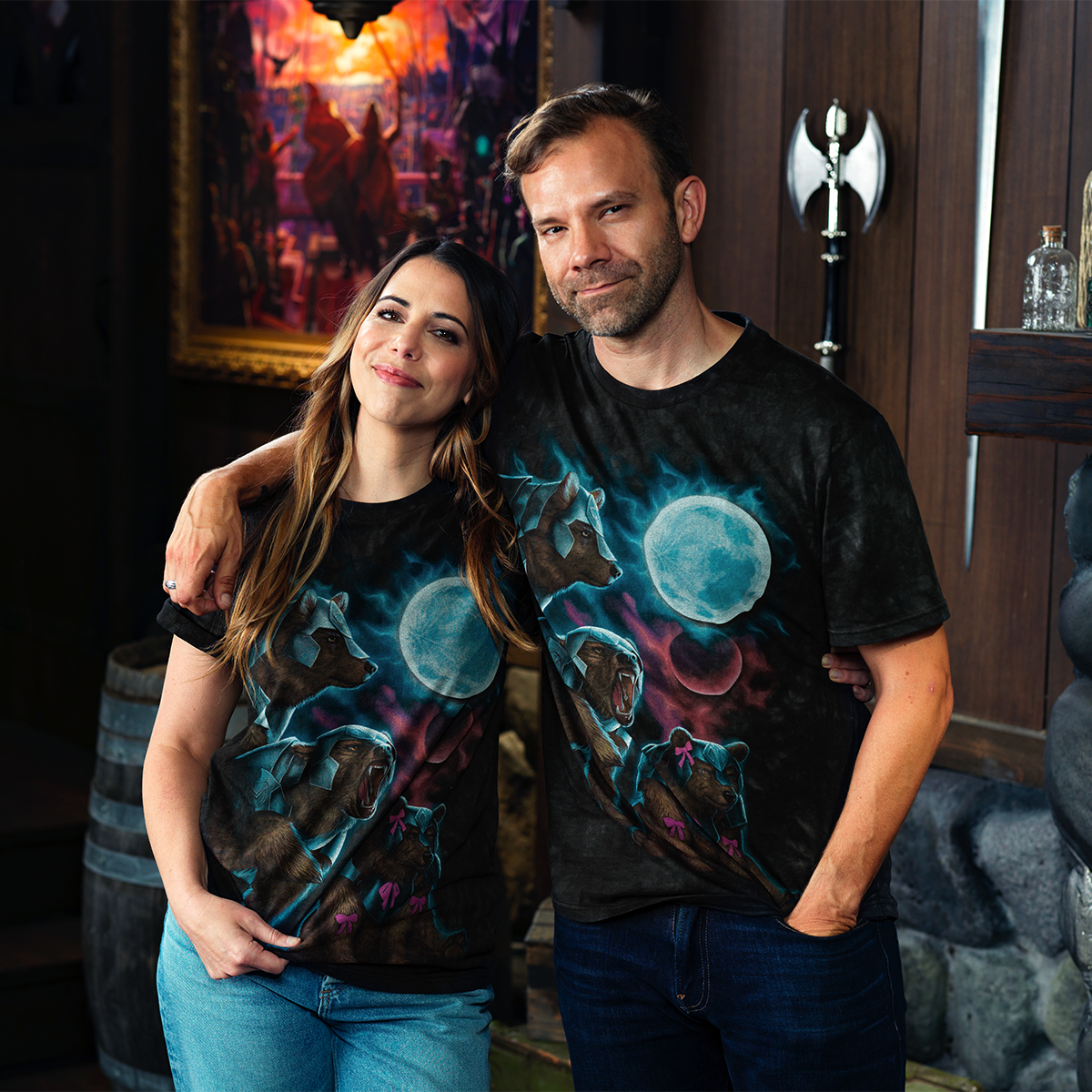 Smiling couple in matching Three Trinket Moon t-shirts featuring moons and armored bears, looking at the camera