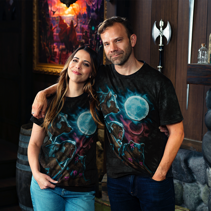 Smiling man and woman in matching black Three Trinket Moon t-shirts with armored bears and blue moons, in a dim fantasy room