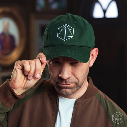 A man tips his dark green Critical Role Dad hat, featuring a white Critical Role d20 and sword logo, looking intently
