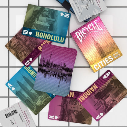 Bicycle "Cities of the World" playing cards (Honolulu, Nairobi) and deck box scattered with a business class ticket