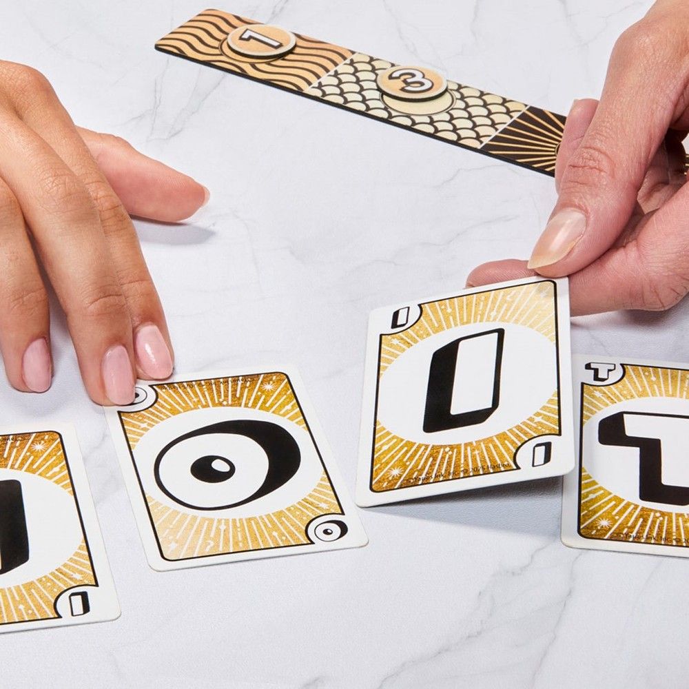 Hands placing gold and black game cards, featuring numbers and symbols, on a white marble surface