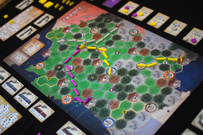 An overhead view of a board game, a hexagonal map of France, with yellow and magenta train route pieces and cards