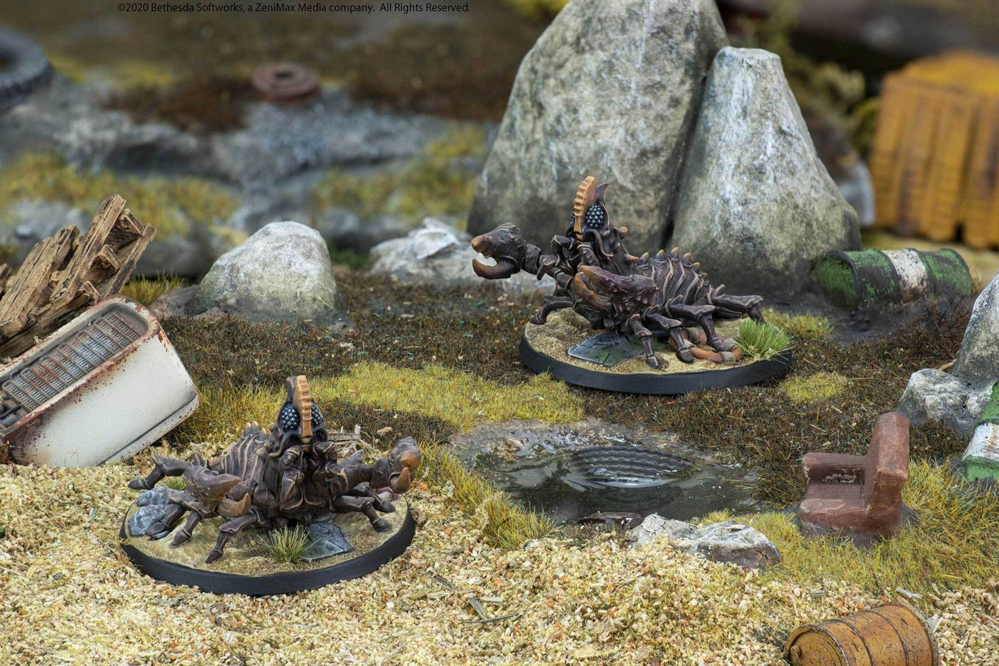 Two armored, scorpion-like miniatures in a wasteland diorama with debris. One raises a claw menacingly