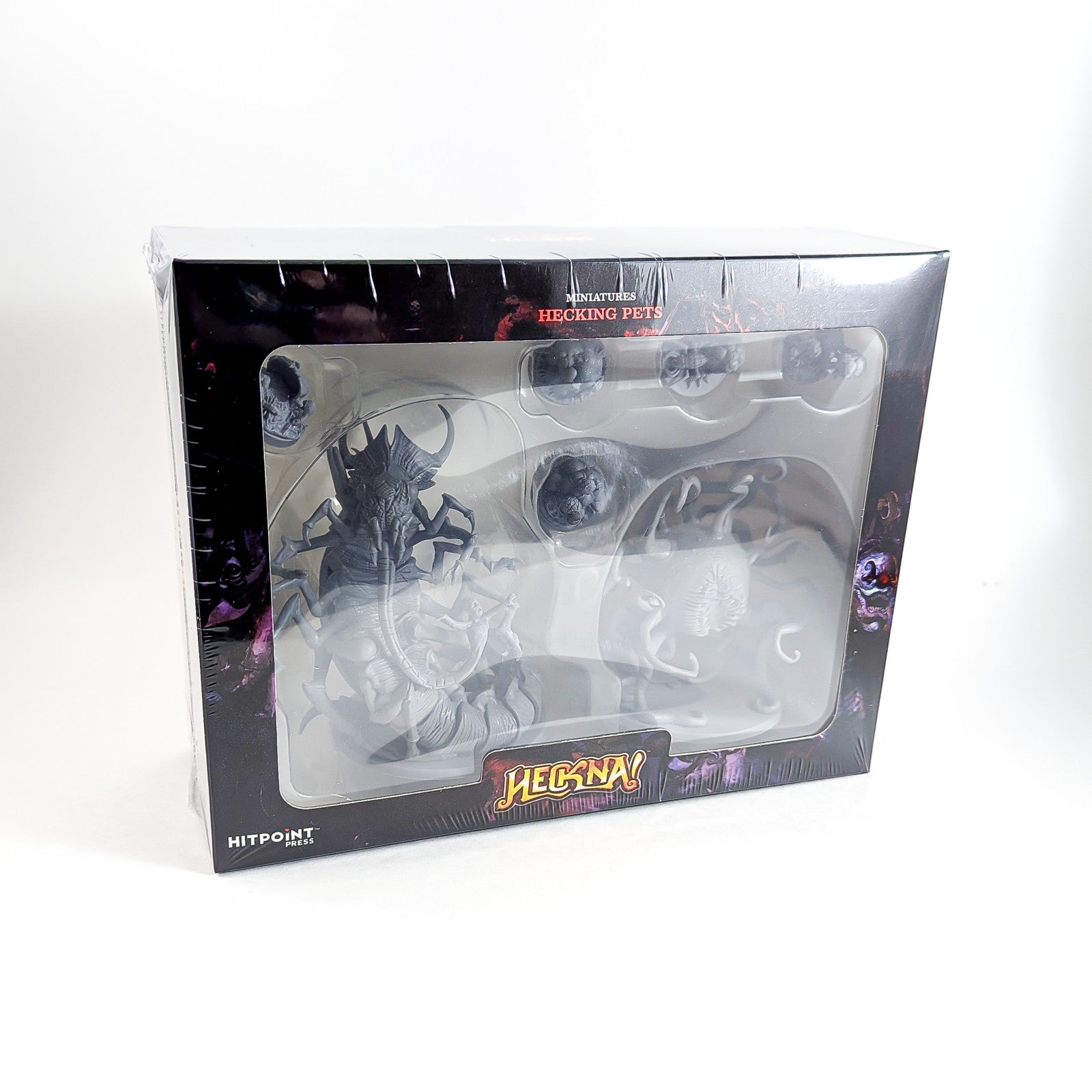 Shrink-wrapped box of "Heckna! Hecking Pets" miniatures: a large dark grey horned creature and several smaller unpainted pets.