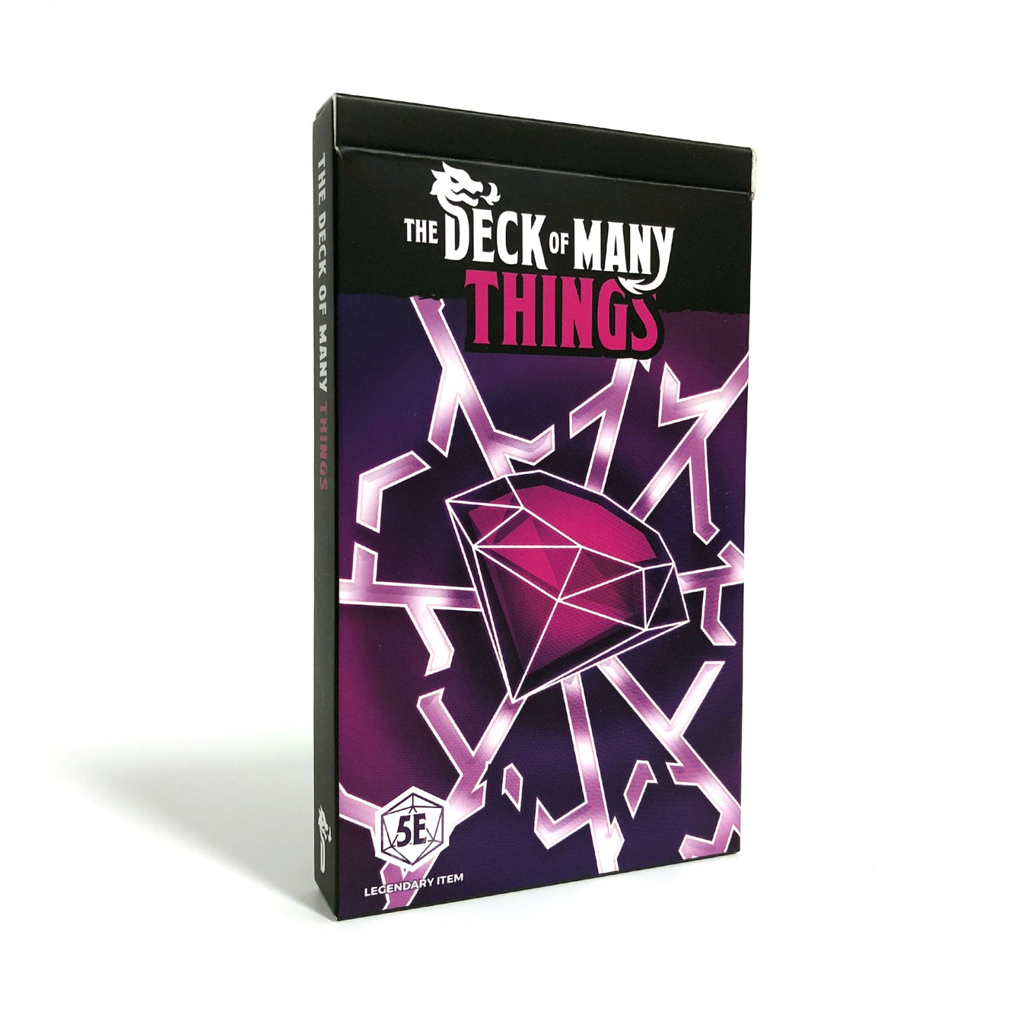 A purple and black box for "The Deck of Many Things" (5E) stands upright, featuring a large pink diamond and abstract geometric lines