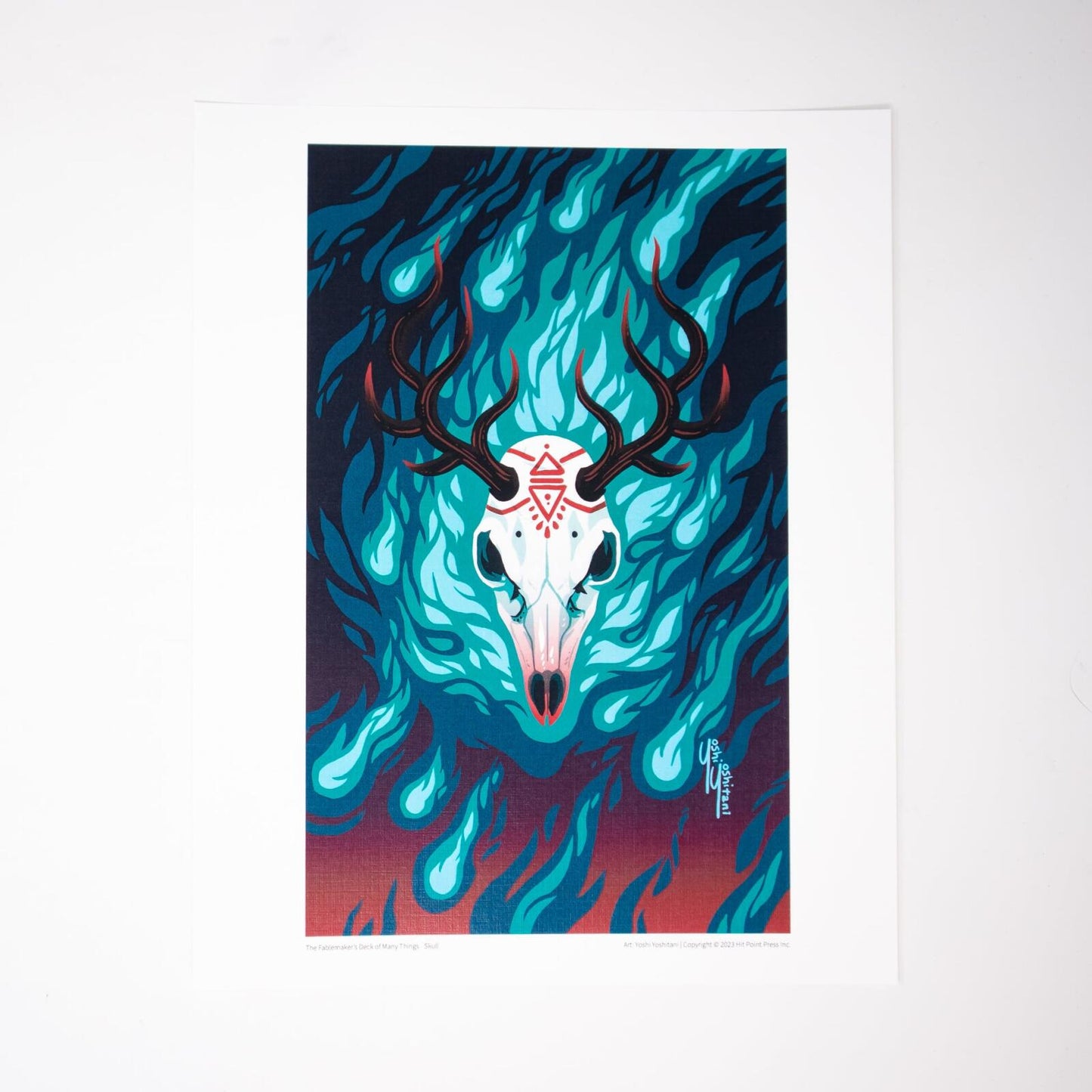 Illustration of a white deer skull with dark antlers and red geometric patterns, surrounded by blue-green flames