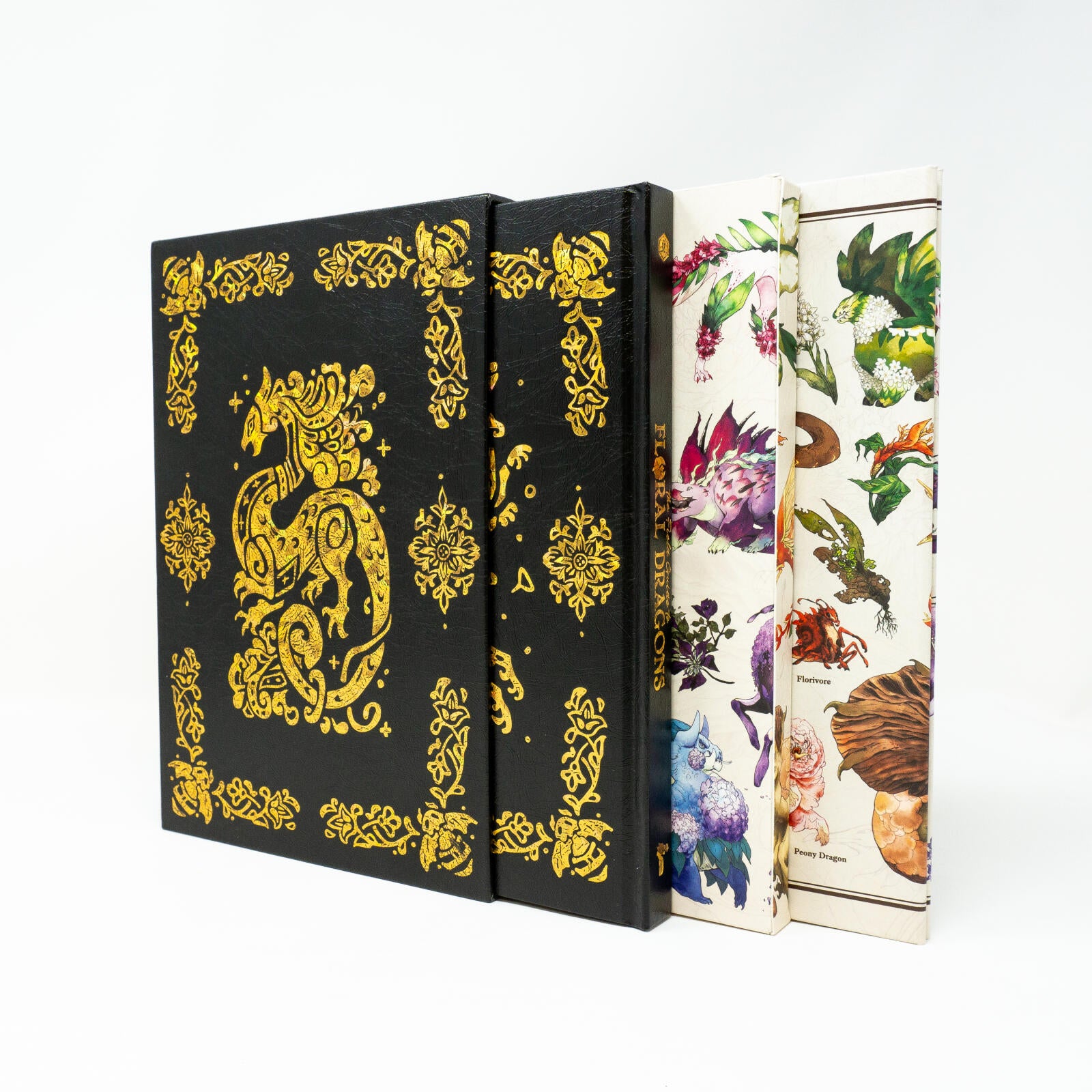 A black book with an intricate gold foil dragon design stands next to two colorful "Floral Dragons" art books