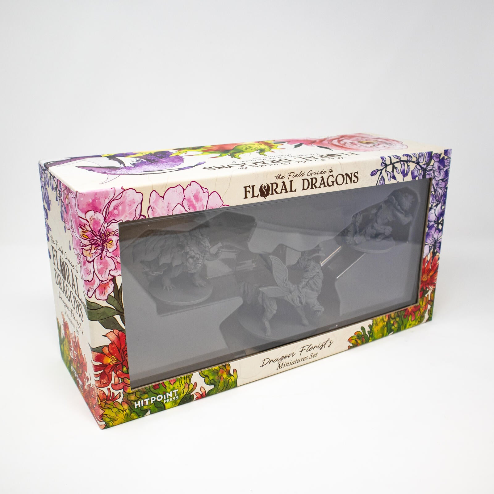 White box for "Floral Dragons" miniatures. Decorated with vibrant floral art, showing three grey dragon figures through a window