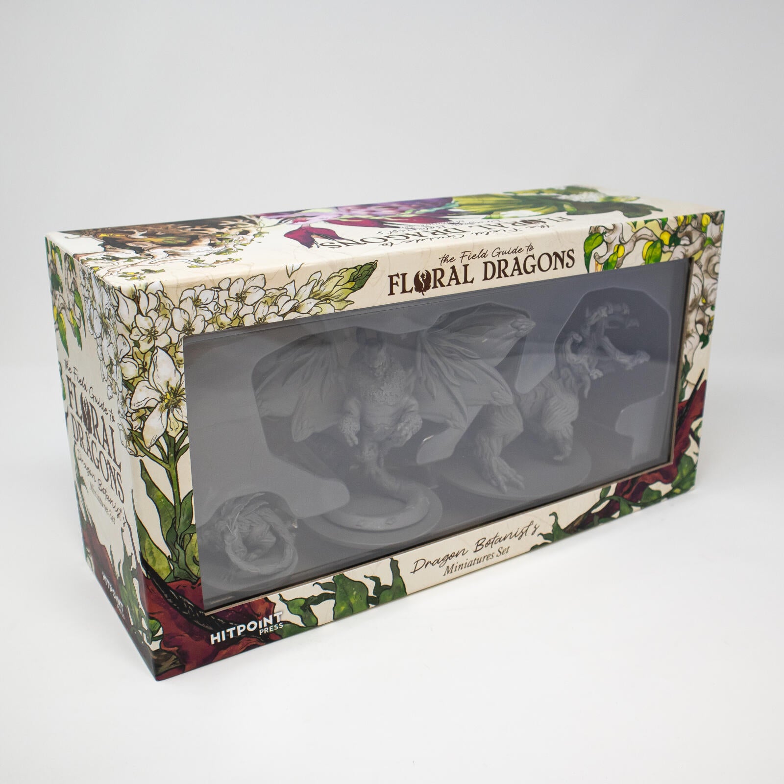 Floral-patterned box for "The Field Guide to Floral Dragons" miniatures, displaying unpainted gray dragon figures
