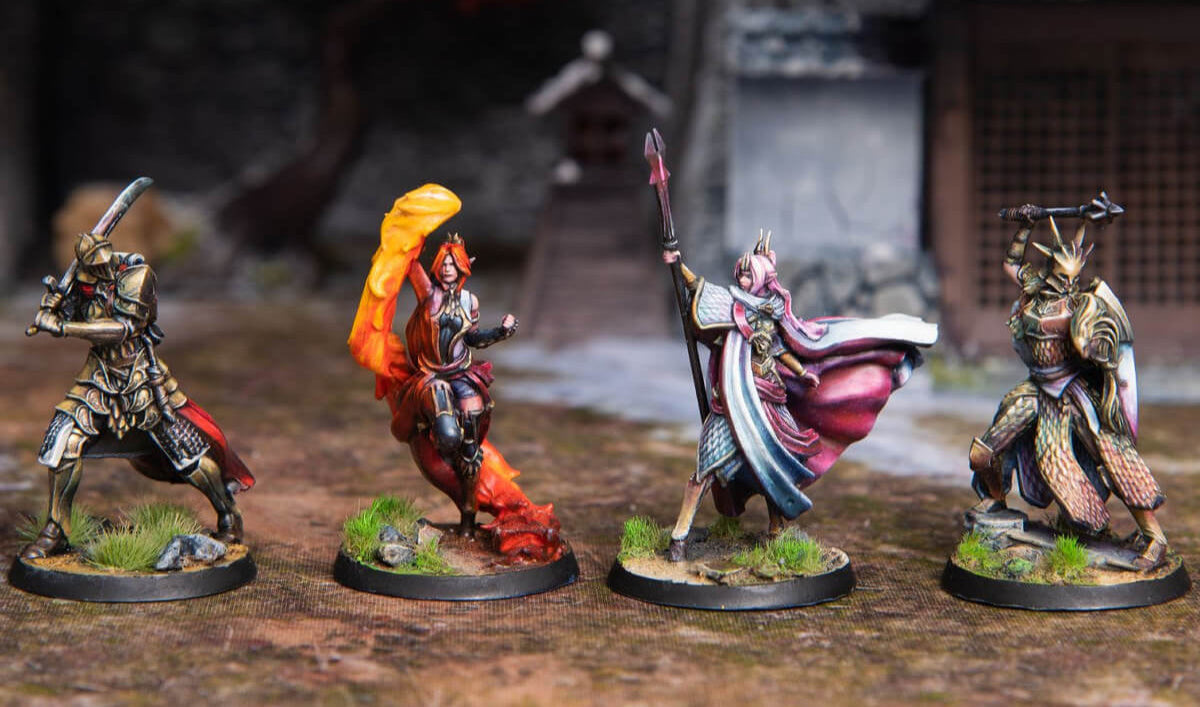 Four painted fantasy miniatures: two armored warriors poised to strike, a fiery sorceress, and a staff-wielding mage