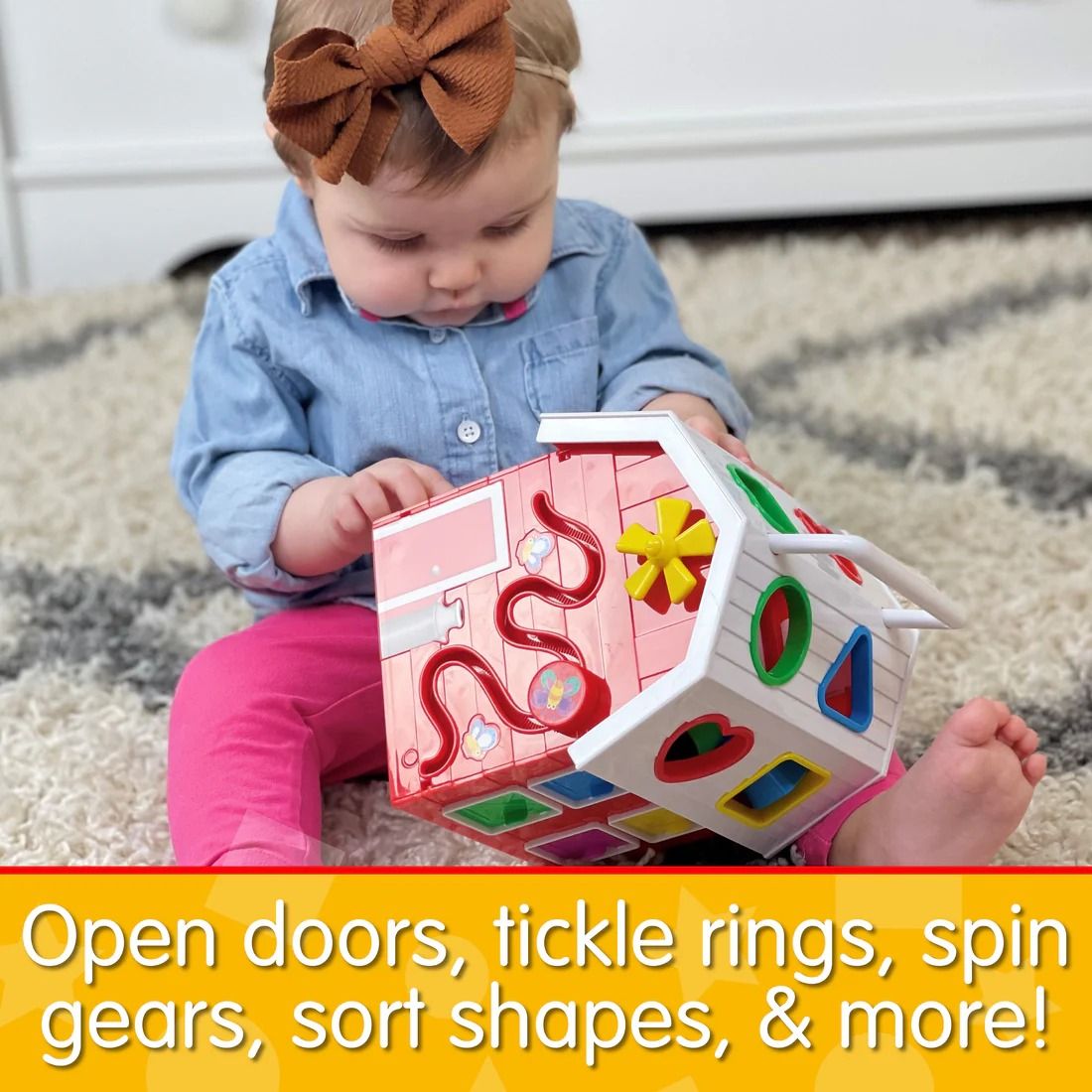 Baby girl playing with a pink and white activity cube toy house, featuring shape sorters, gears, and bead mazes