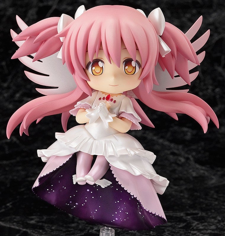 A chibi Ultimate Madoka figurine with pink hair, white wings, a ruffled white dress with starry purple underside, holding a white item
