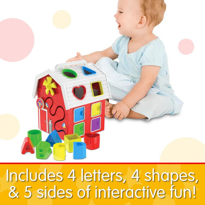 Smiling baby plays with a red barn shape sorter activity toy, featuring colourful blocks and letters