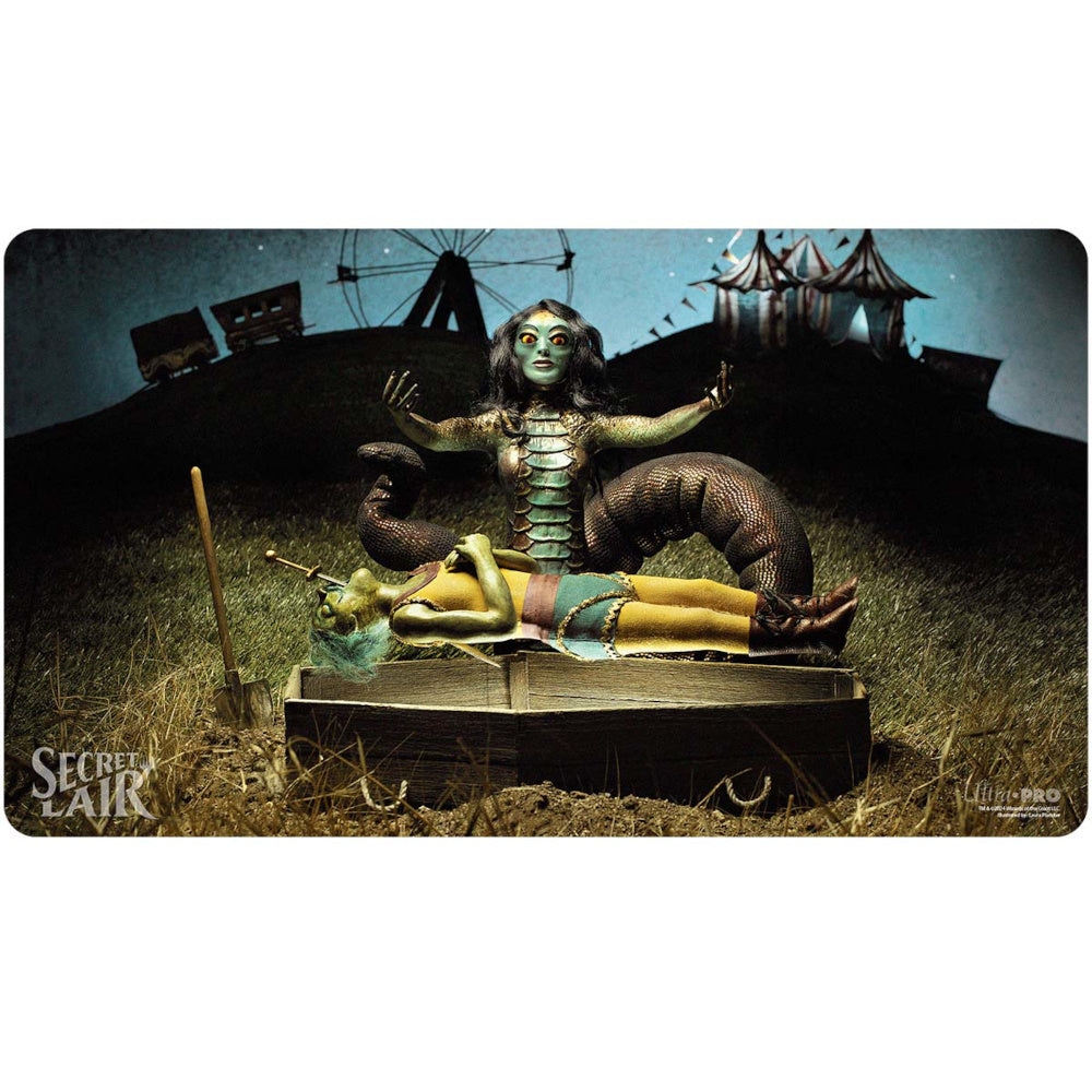 A green-skinned snake-woman with glowing eyes and outstretched arms stands over a motionless jester on a book, in a dark carnival