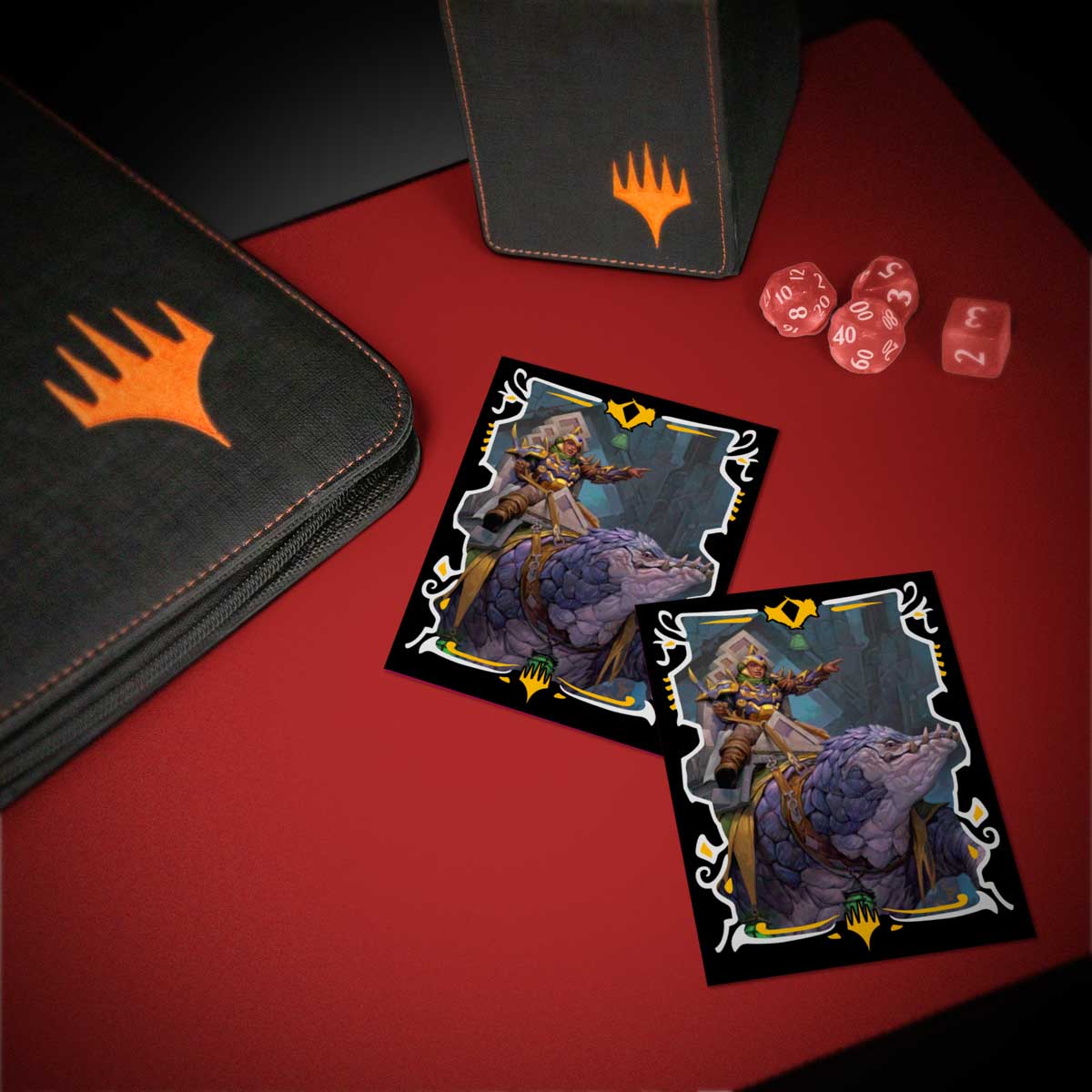 Two Magic: The Gathering cards depicting a warrior on a purple beast, with a binder, deck box, and red dice on a red playmat