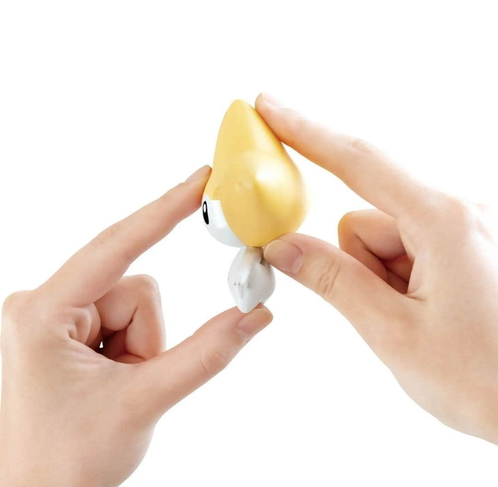 Small yellow and white Jirachi Pokemon figure held by two hands on a white background