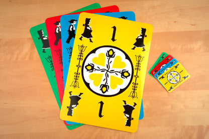 Colorful Dutch Blitz JUMBO! game cards fanned out on a light wooden table. A yellow card with '1', character silhouettes, and a heart design is prominent