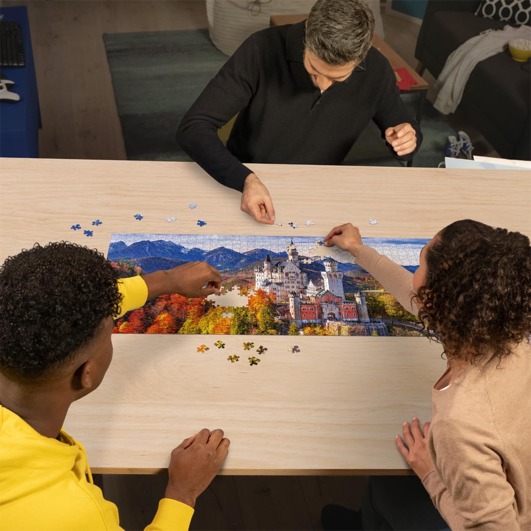 Three people assemble the 1000-piece Castello Bavaria jigsaw puzzle, which shows the picturesque German castle amid colorful fall foliage