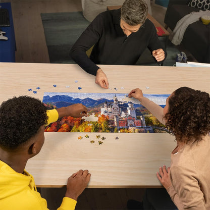 Three people assemble the 1000-piece Castello Bavaria jigsaw puzzle, which shows the picturesque German castle amid colorful fall foliage