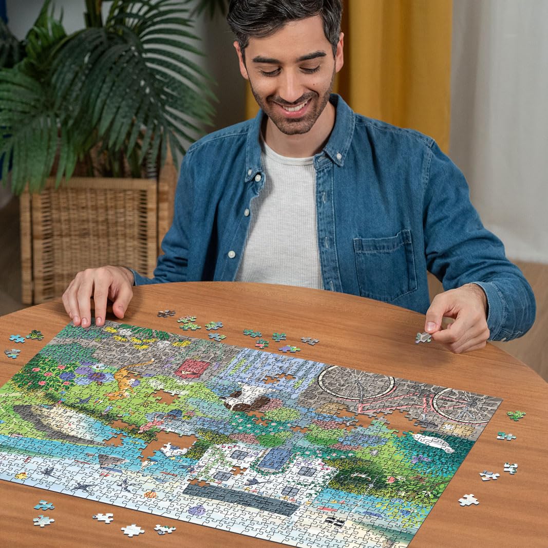 A smiling man connects a piece to the large, colorful Ravensburger Coastal Cottage 1000 piece jigsaw puzzle on a smooth wooden surface