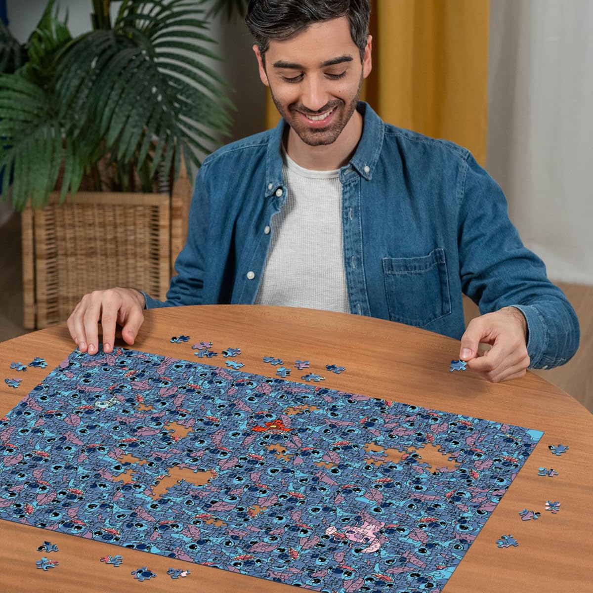 A smiling man assembles a nearly complete Ravensburger Disney Stitch Challenge 1000 piece jigsaw puzzle featuring numerous blue Stitch figures