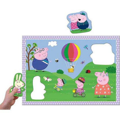 Ravensburger Peppa Pig floor puzzle featuring characters like Daddy Pig and Peppa on bikes near a hot air balloon, with an oversized bunny piece held ready for insertion
