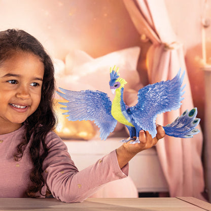 A smiling young girl holds a blue and yellow Schleich Magic Peacock toy with large wings and a fanned tail
