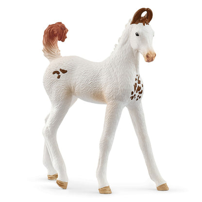 A toy white foal with brown spots, mane, tail, and ears, standing on a white background