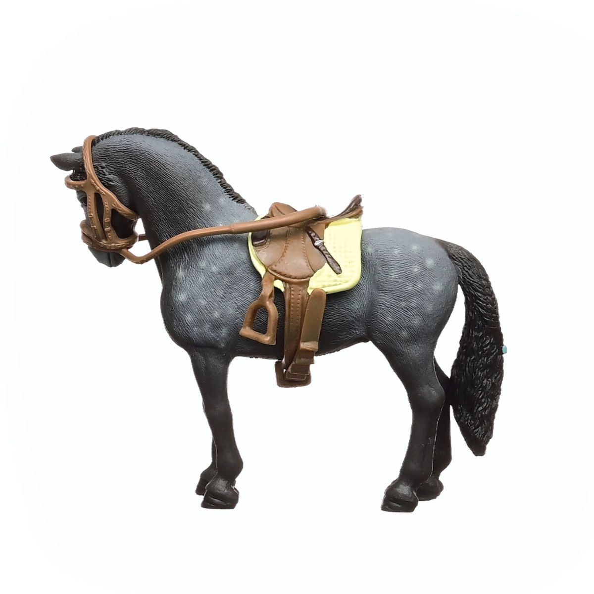 A Pura Raza Espanola mare toy with a dapple grey coat stands facing left, wearing a brown saddle with a yellow pad and a brown bridle